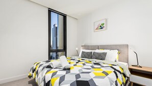 Ein modernes Hotelzimmer mit einem großen Bett, einem Nachttisch, einem Schreibtisch, einem Sessel und einem Fenster mit Blick auf die Stadt.