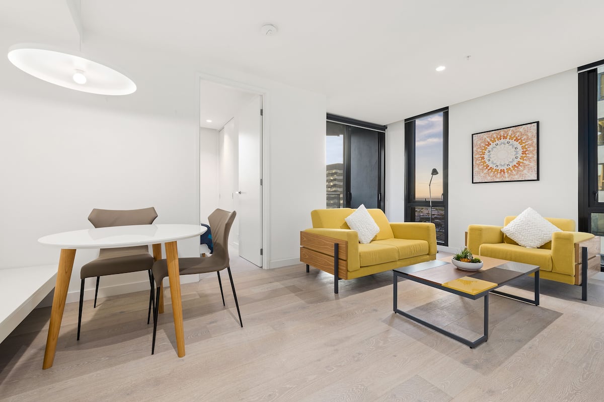 A modern living room with a white dining table, two yellow sofas, and a coffee table.