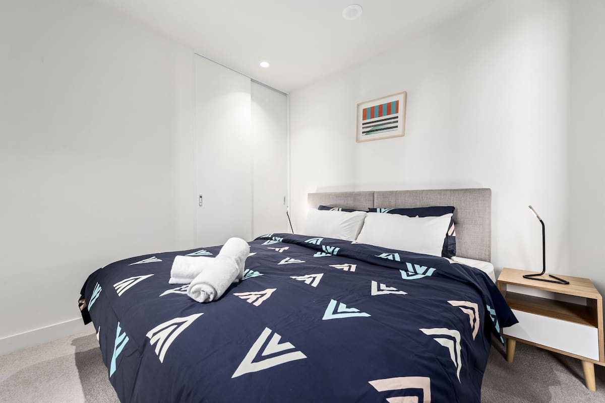 A modern bedroom with a bed, a bedside table, and a wall-mounted artwork.