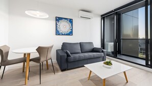 Ein modernes Wohnzimmer mit einem grauen Sofa, zwei Sesseln, einem weißen Tisch und einem großen Fenster mit Blick.
