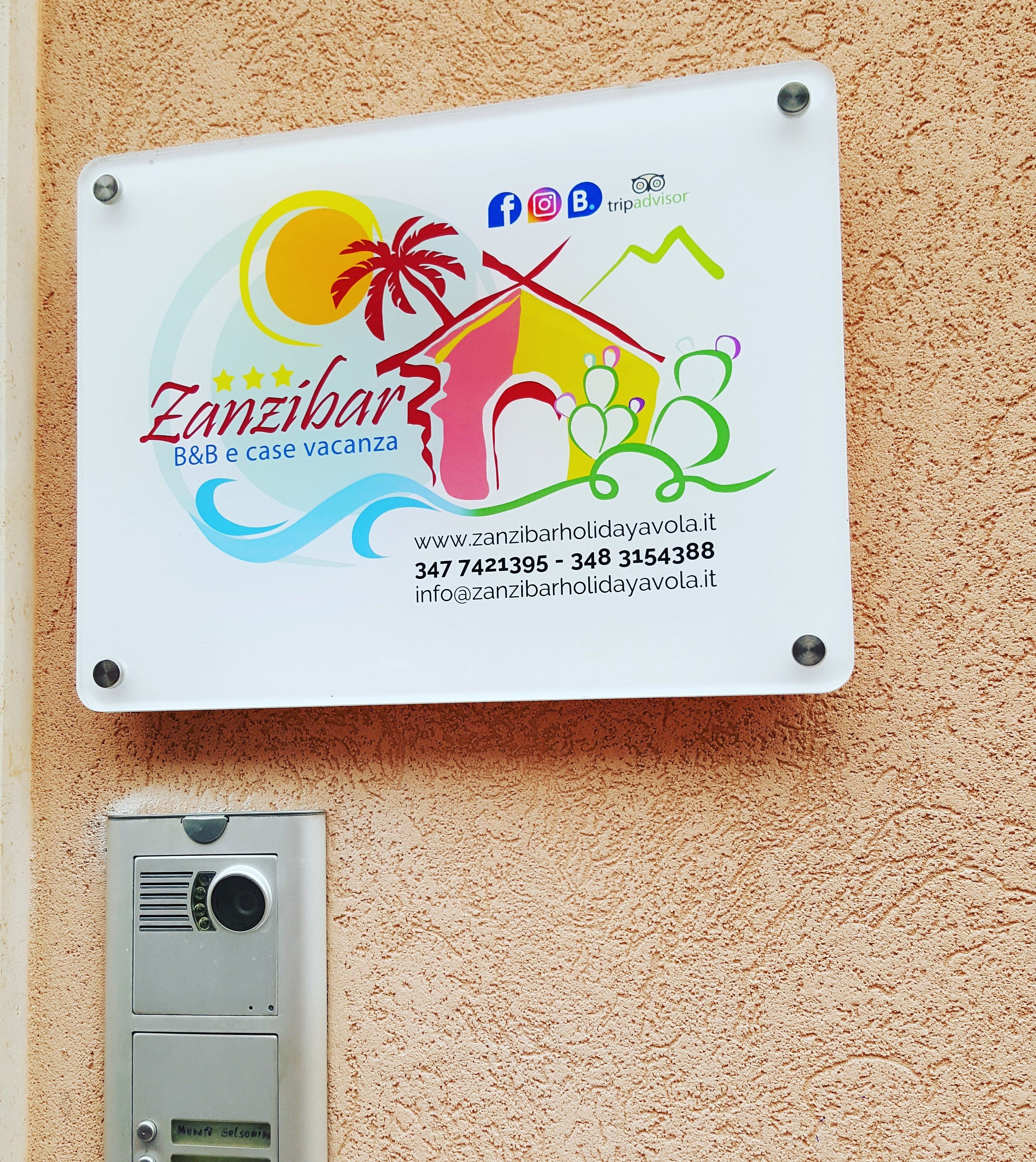 Eine an der Wand befestigte Schilder für eine Ferienvilla in Sansibar mit Kontaktinformationen und Social-Media-Symbolen.