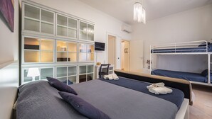 Ein Hotelzimmer mit einem großen Bett, einem Einzelbett, einem Schreibtisch mit Stuhl und einem an der Wand befestigten Fernseher.