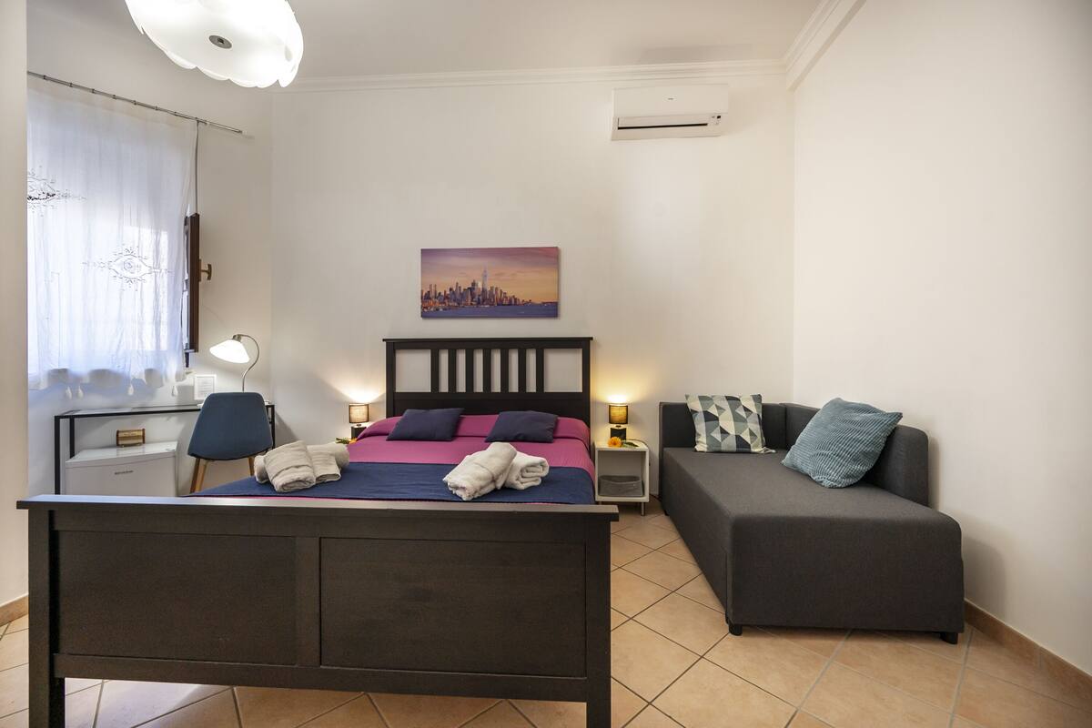 Ein Schlafzimmer mit Bett, Nachttischen, einer Couch, einem Gemälde und einer Klimaanlage.