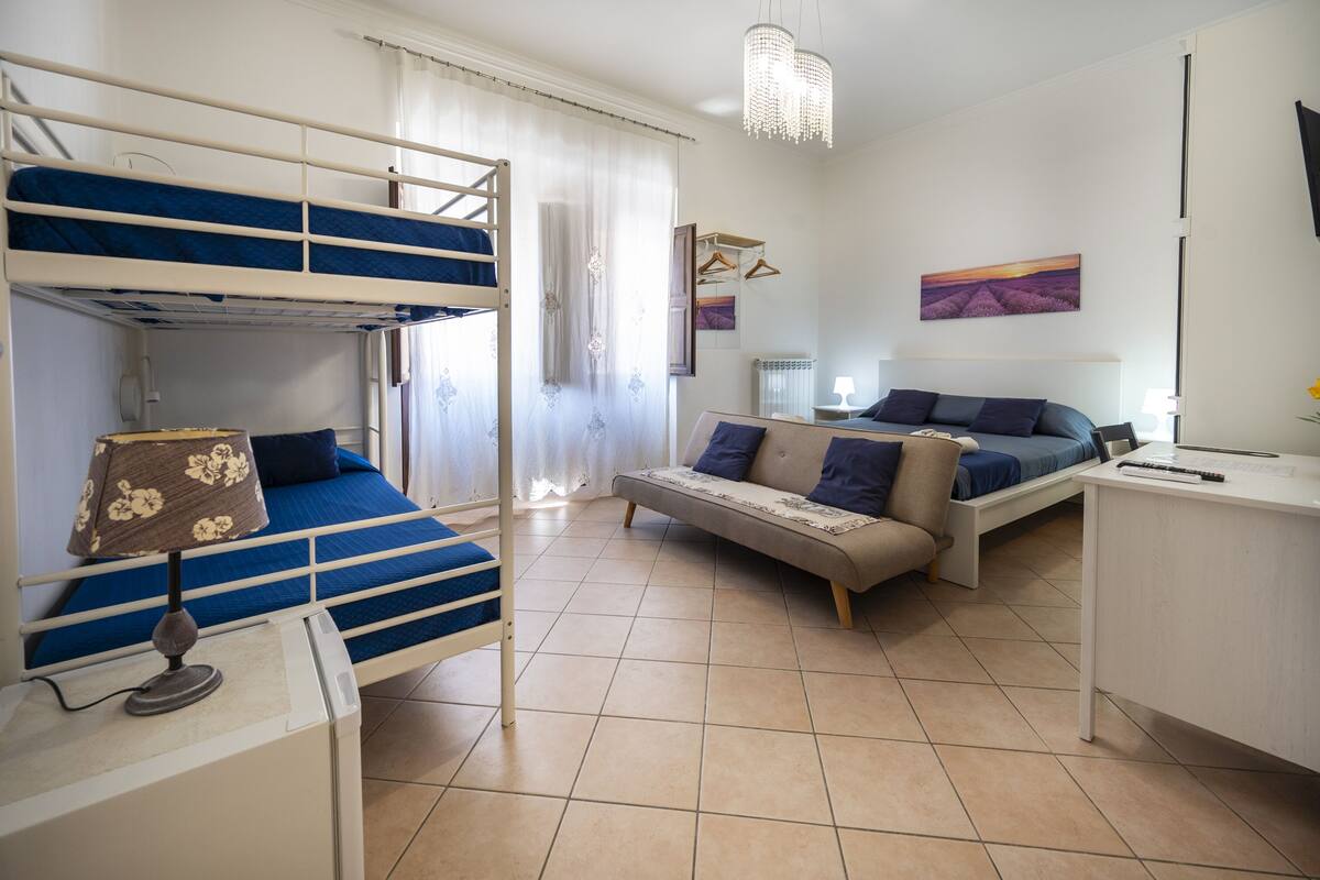 Ein Schlafsaalzimmer mit Etagenbetten, einer Schlafcouch, einem Schreibtisch und einer Pendelleuchte.