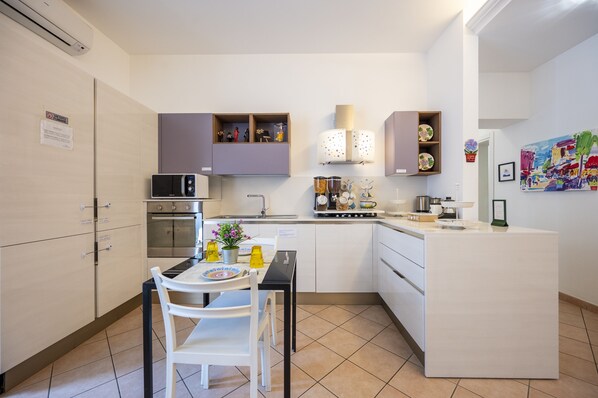 A modern kitchen with white cabinetry, a built-in microwave, and a dining area with a table and chairs.