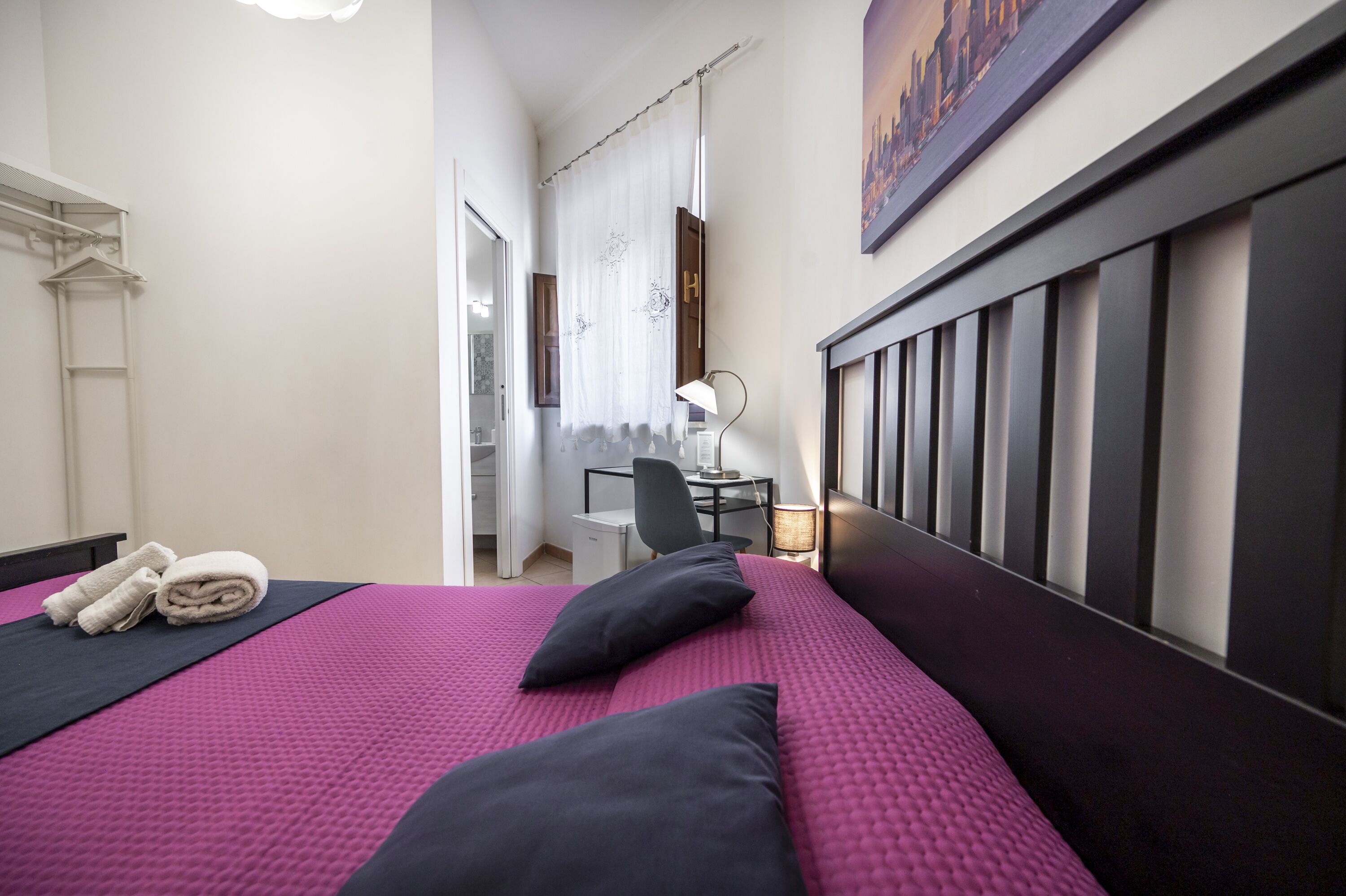 A hotel room with a bed, a desk, a chair, and a painting on the wall.