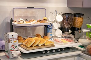 Ein Frühstücksbuffet mit verschiedenen Backwaren, Brot und einer Kaffeestation.