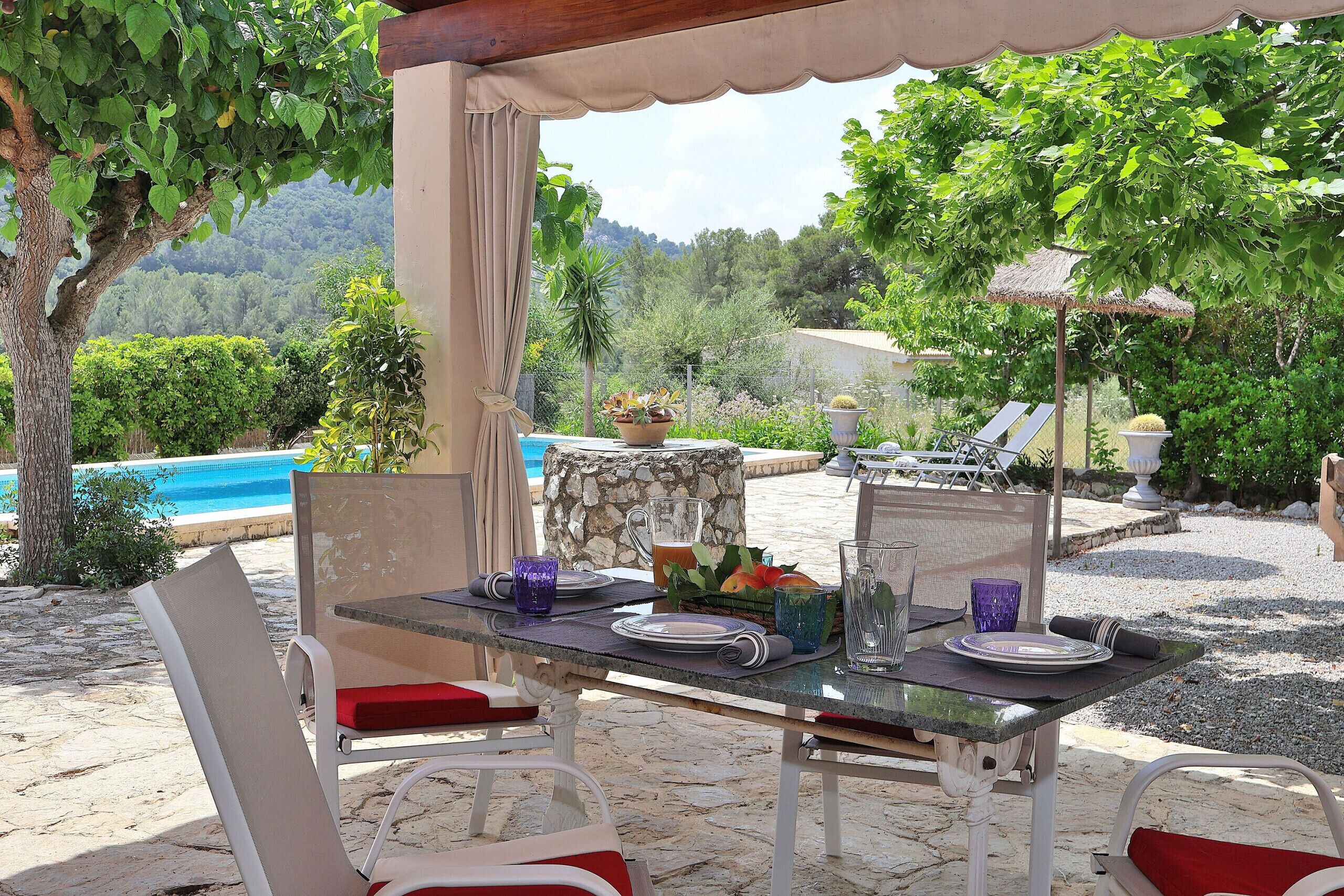 Un espace de restauration en plein air avec une table dressée pour deux personnes, une table en pierre et une vue sur la piscine et les montagnes.