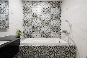 A bathroom with a mosaic tile wall, a white bathtub, and a black countertop. - 3BRs Luxury Apartment Cityview (Ho Chi Minh City)