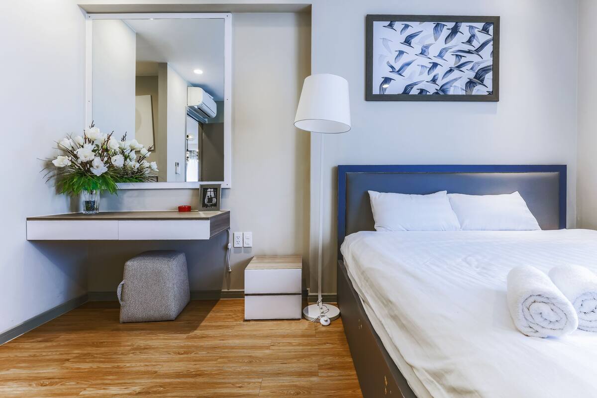 A hotel room with a bed, bedside table, mirror, and a wall-mounted picture.