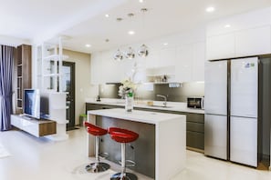 A modern kitchen with a central island, bar stools, a refrigerator, and a built-in oven. - 3BRs Luxury Apartment Cityview (Ho Chi Minh City)