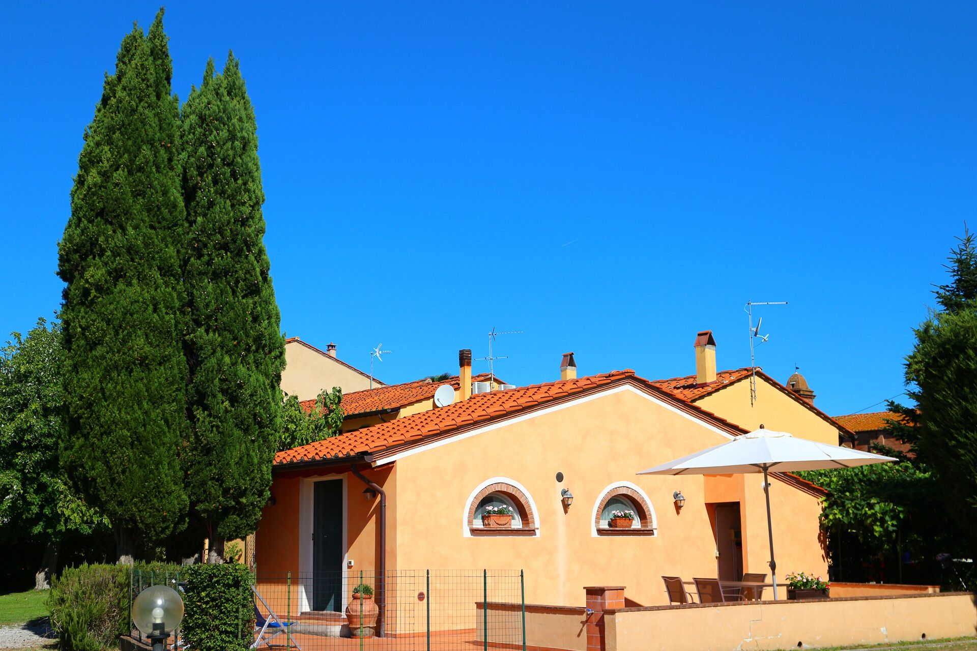 Un bâtiment à deux étages, avec un toit recouvert de tuiles rouges, un grand arbre devant et un ciel bleu dégagé.
