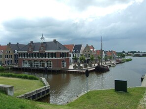 En byggnad som ligger vid en kanal och har en traditionell arkitektonisk stil, med ett markant torn och stora fönster.
