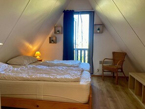 A bedroom with a bed, a chair, a lamp, and two wall-mounted shelves with plants.