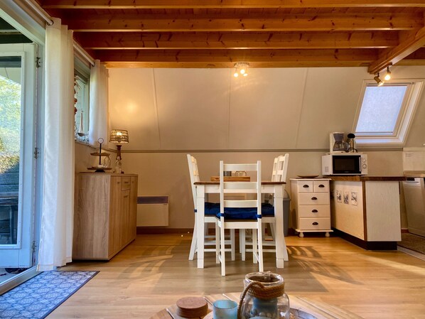 Una cocina acogedora con vigas de madera, una mesa de comedor con sillas, un microondas y un ventanal pequeño.