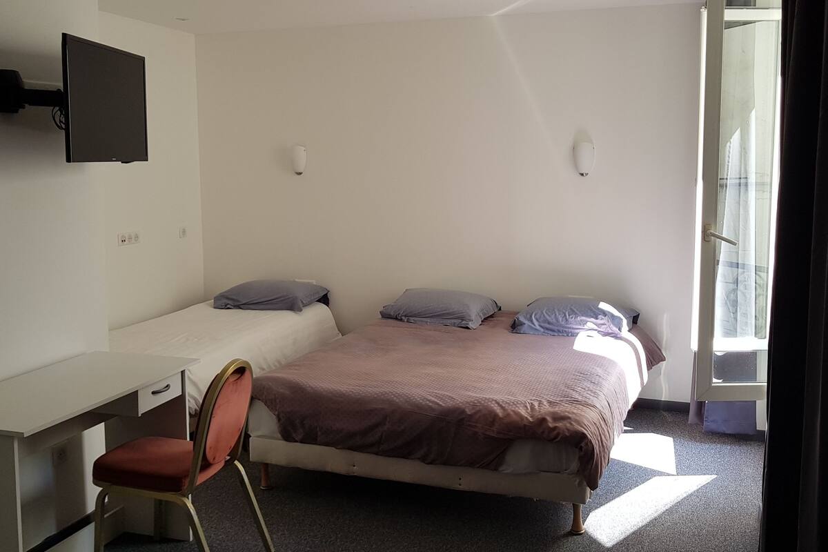 Quarto com cama, escrivaninha, cadeira e TV fixada na parede.