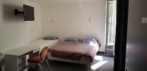 Un dormitorio con una cama, un escritorio, una silla y un televisor instalado en la pared.