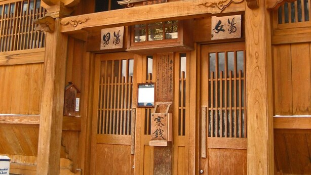 A traditional wooden building with a curved roof and multiple signs with Chinese characters. - Nakajimaya Ryokan (Nozawaonsen)