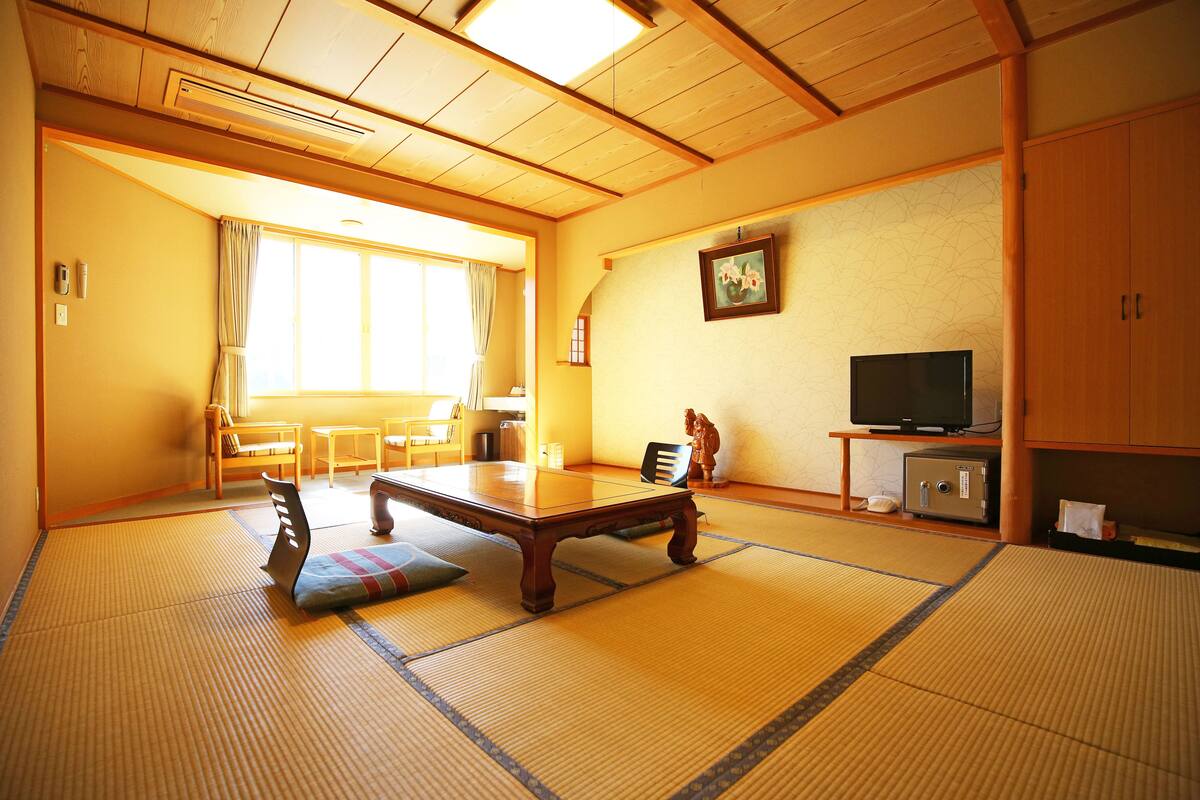 Una habitación japonesa tradicional con suelo de tatami, una mesa de madera baja, un televisor y un armario.