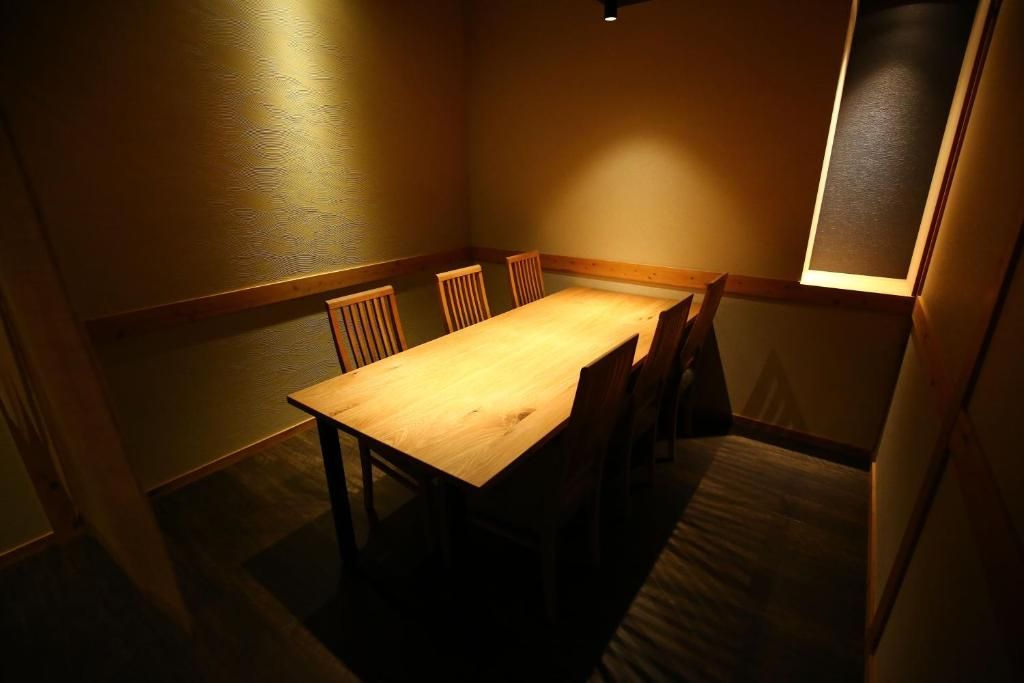 A dining area with a wooden table and chairs, a light fixture on the ceiling, and a window on the right wall.
