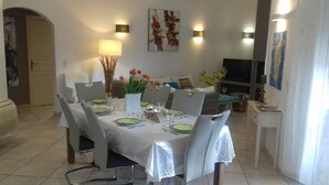 Un coin repas avec une table dressée pour quatre personnes, entourée de chaises, et agrémenté d’un téléviseur et d’œuvres d’art aux murs.