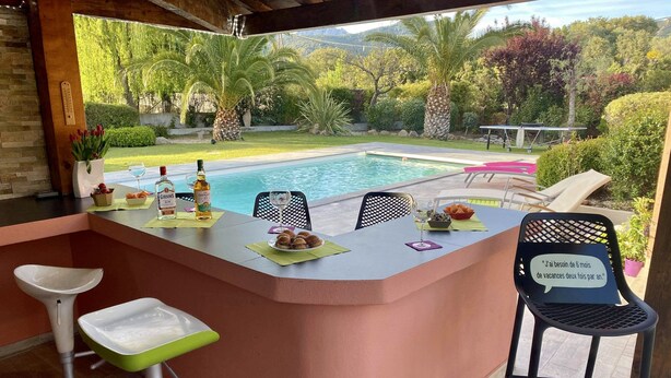 Un bar situé au bord de la piscine, offrant une vue sur la piscine et le jardin.
