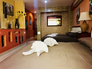 Habitación de hotel con cama, mesita de noche, lámpara y televisor montado en la pared.