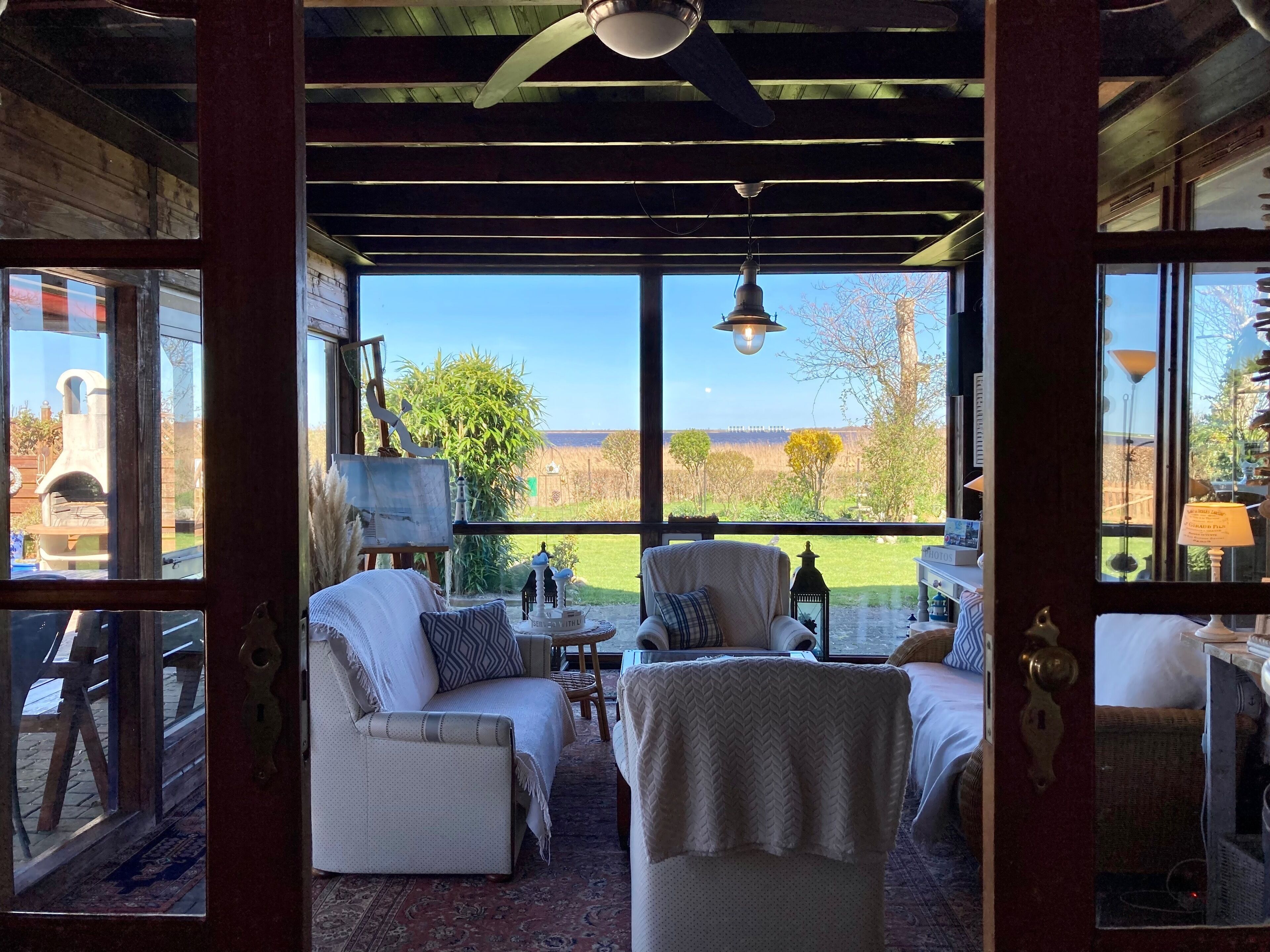 Een gezellig ingerichte kamer met uitzicht op het landschap, met een bank, fauteuil en een kleintje tafeltje met decoratieve objecten.