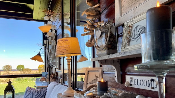 Una habitación acogedora con un sofá de mimbre, un letrero que dice 'WELCOME', adornos y vistas al exterior.