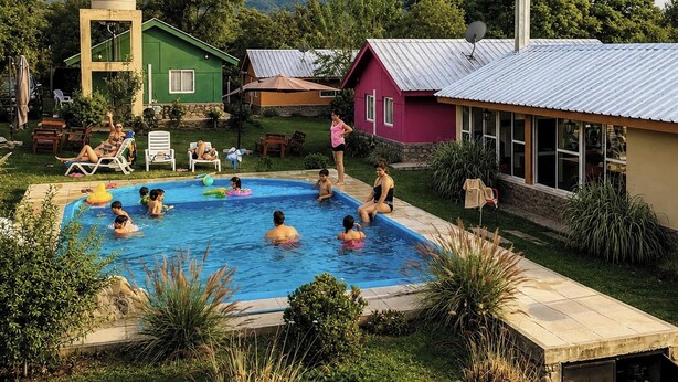 Una piscina rodeada de casas, con gente nadando y descansando.