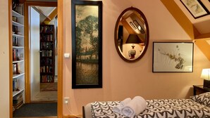 Une pièce chaleureuse avec une bibliothèque, un tableau, un miroir et un lit recouvert d’une literie à motifs.