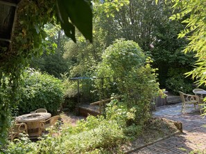 A garden patio with a round table and chairs, surrounded by lush greenery and a wooden fence. - 5 pers - Equipped house Gudrun with sauna - Dogs are welcome (Anjum)