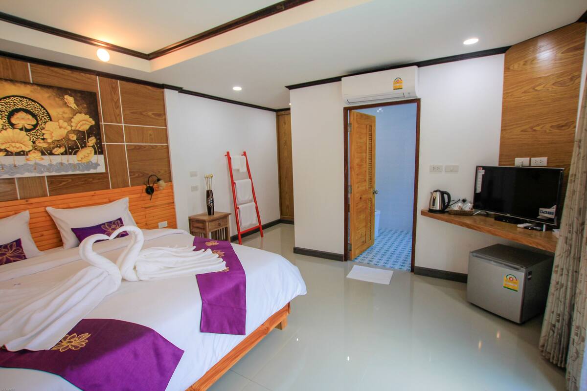 Habitación de hotel con una cama bien hecha, un televisor, un refrigerador pequeño y un cuadro en la pared.