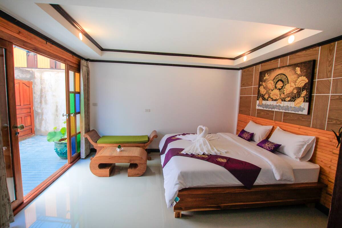 Un dormitorio con una cama, un banco de madera, una mesita pequeña y una planta en maceta.
