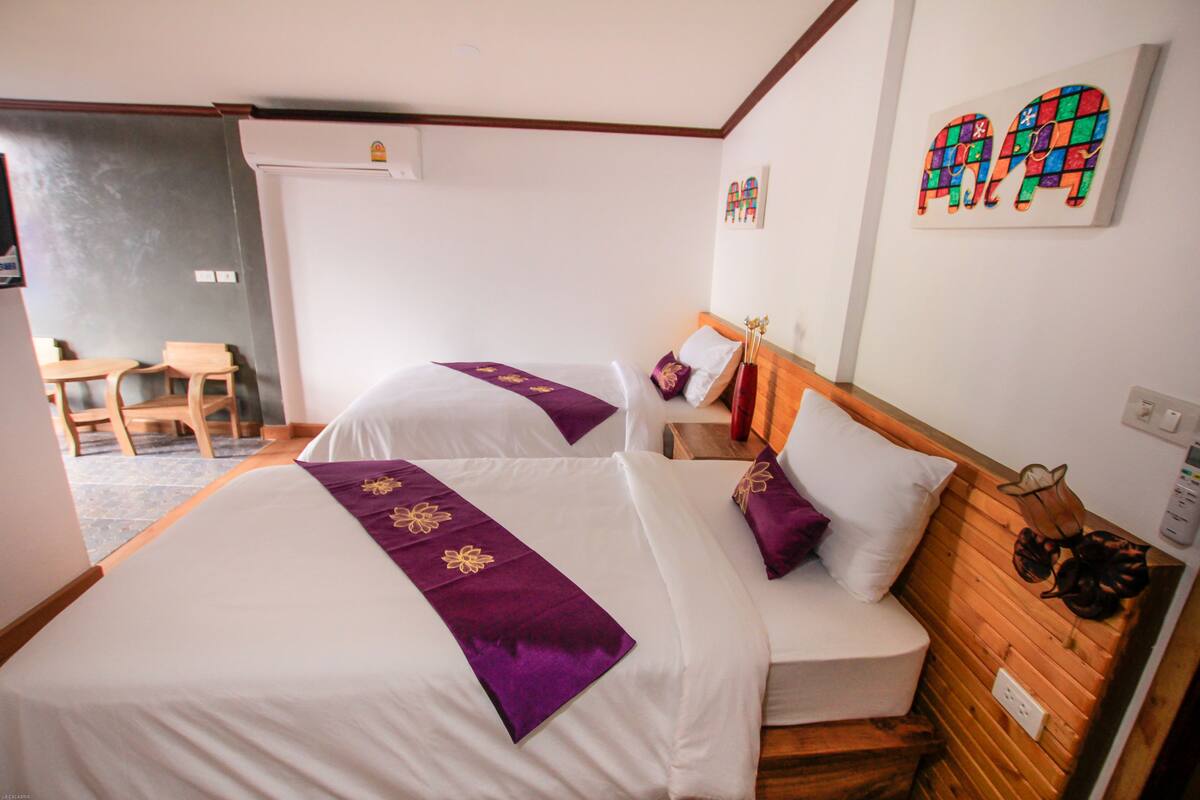 Habitación de hotel con dos camas, cabecero de madera, una mesita y una silla.