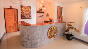A reception area with a curved counter, a decorative wall piece, a potted plant, and a wooden door. - Amethyst Boutique Hotel Fisherman's Village (Koh Samui)