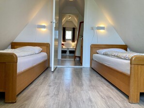 A room with two wooden beds, a small table, and a mirror.