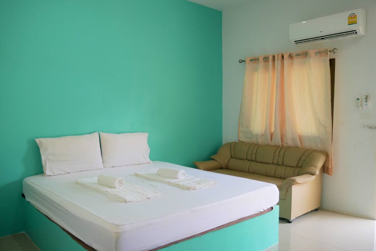 A room with a bed, a sofa, a curtain, and an air conditioning unit.