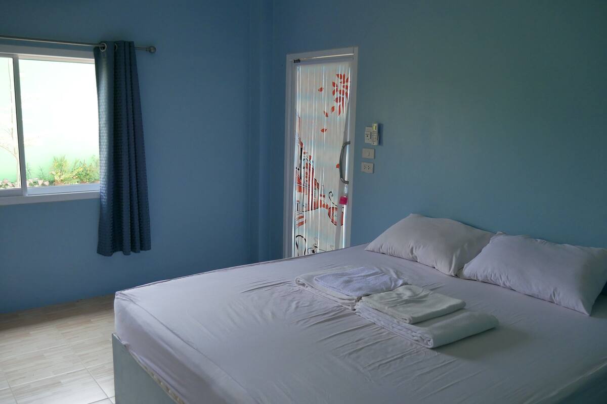 A bedroom with a bed, a window with curtains, and a door with a patterned curtain.