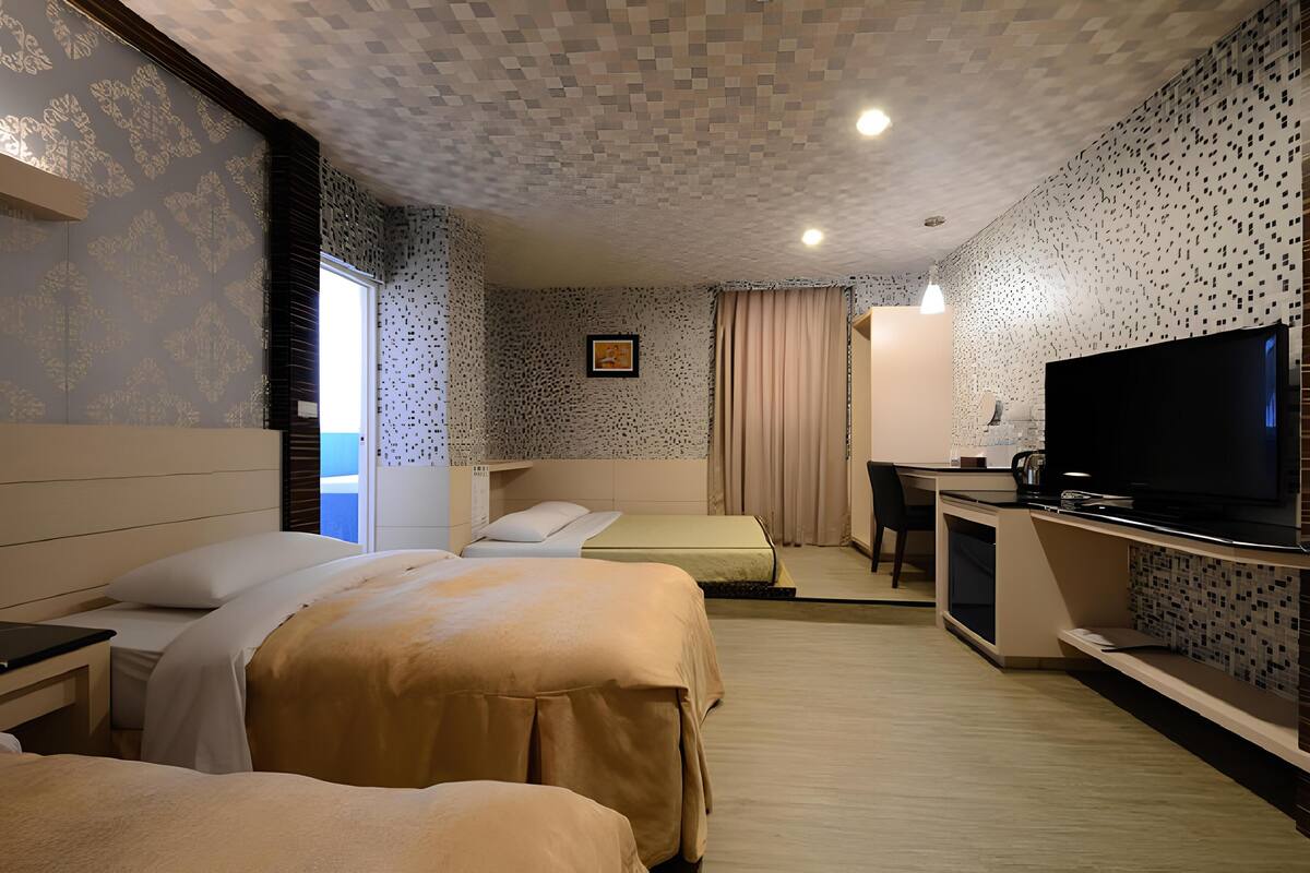 A hotel room with two beds, a desk, a television, and a window with curtains.