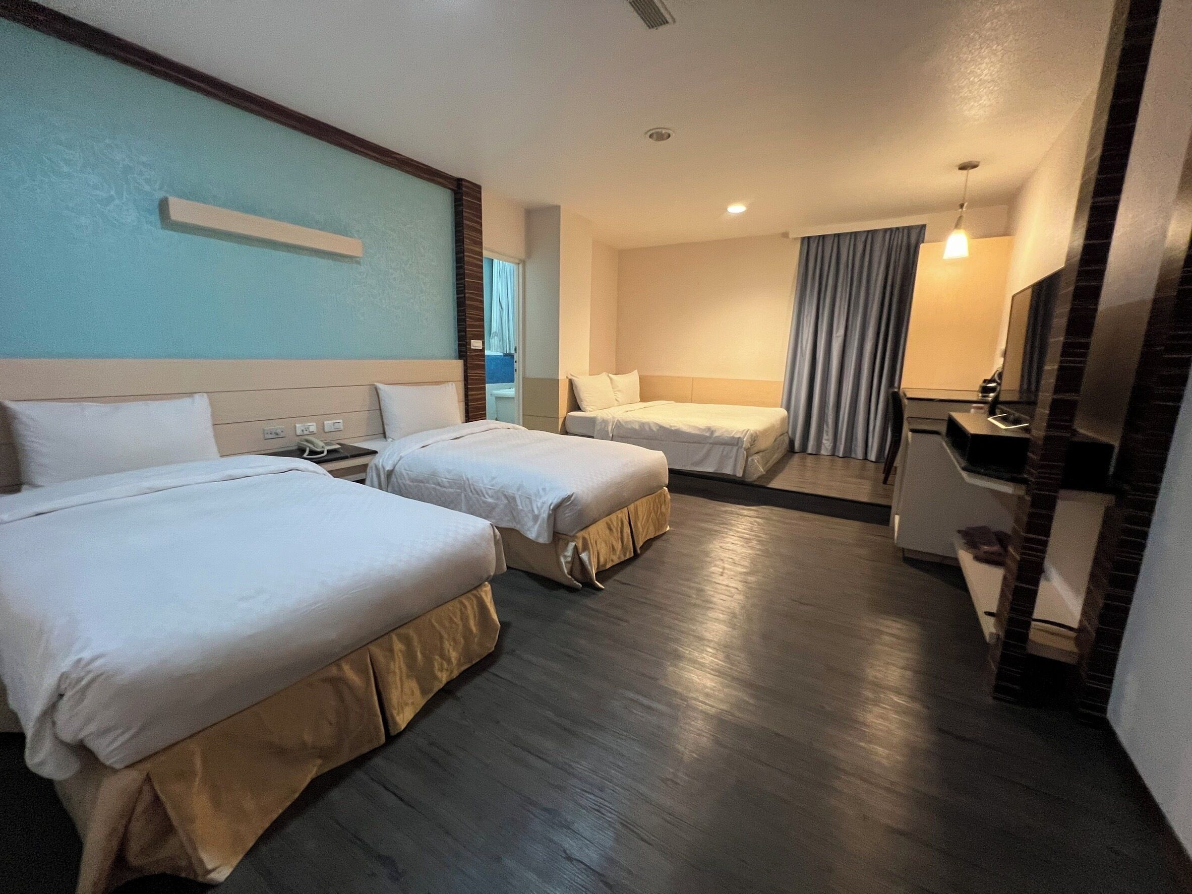 A hotel room with two beds, a desk, a mirror, and a small kitchenette.