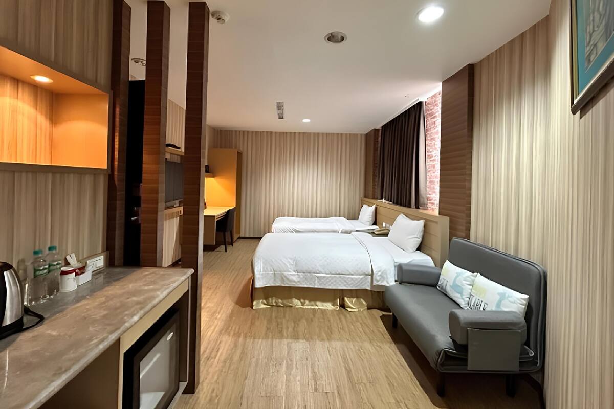 A hotel room with two beds, a desk, and a sofa.