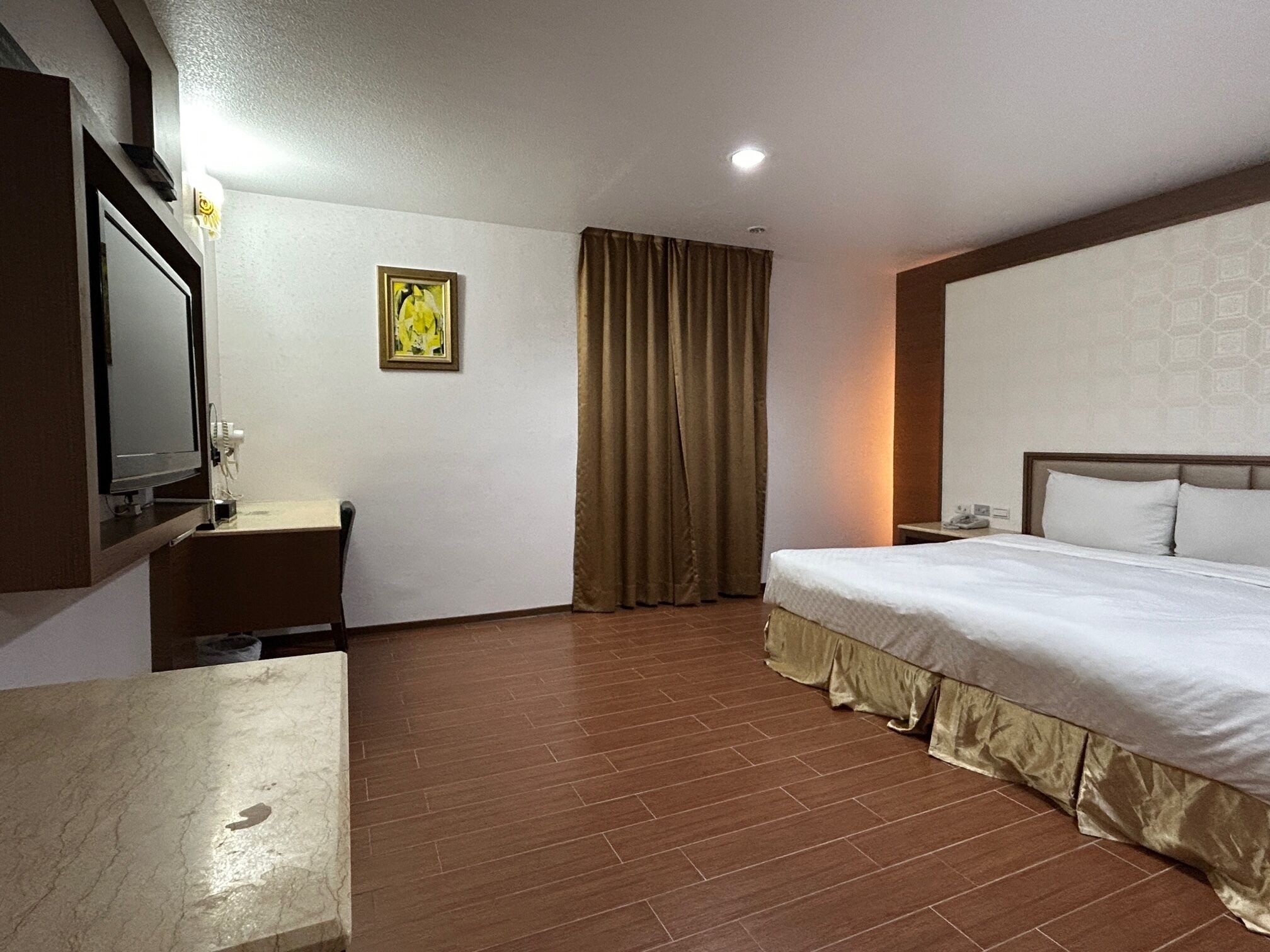 A hotel room with a bed, a desk, a television, and a window with curtains.