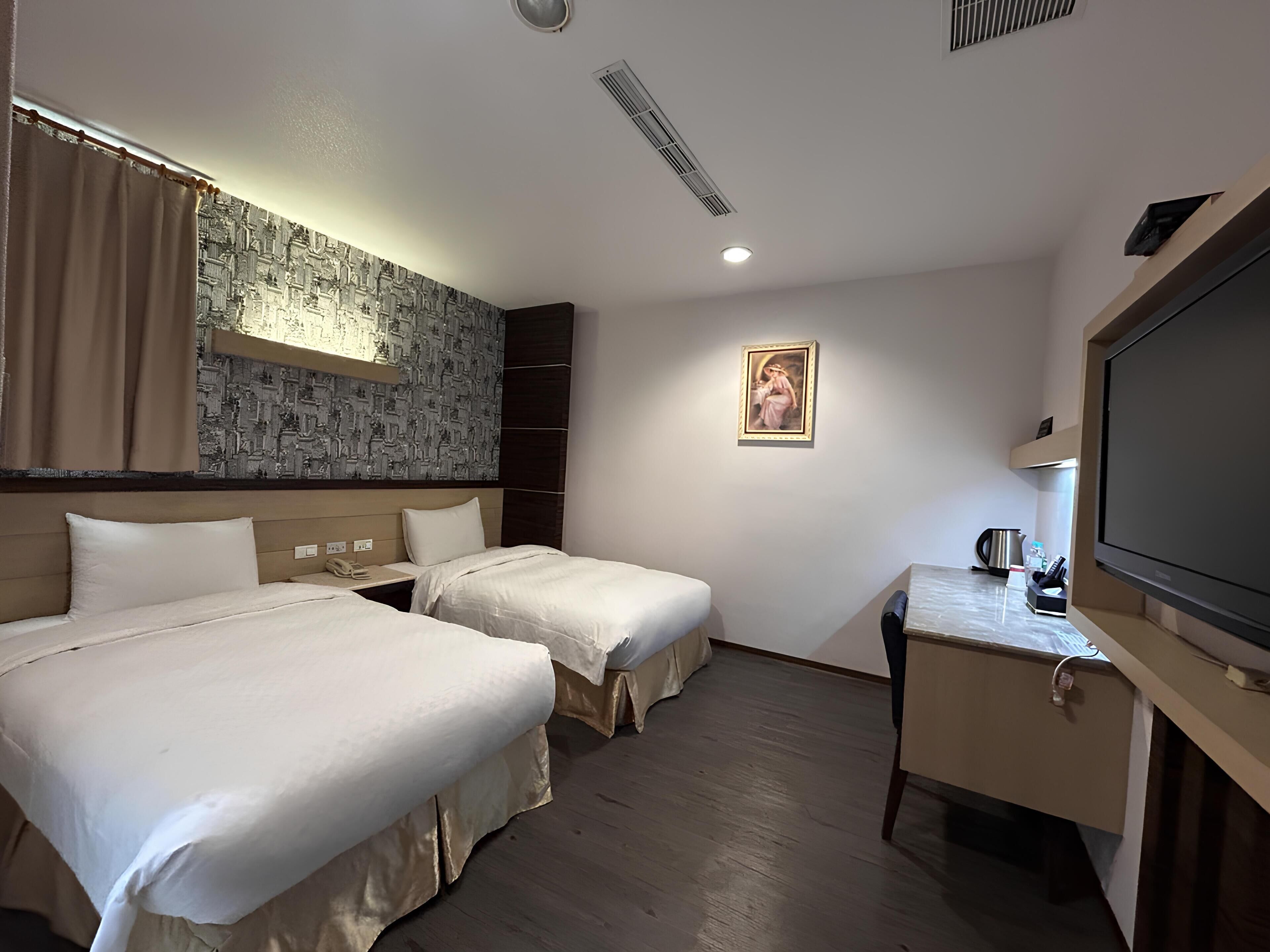 A hotel room with two beds, a desk, a television, and a painting on the wall.