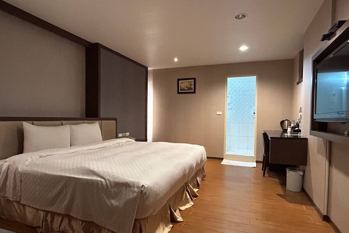 A hotel room with a large bed, a desk, a chair, a television, and a door leading to a balcony.