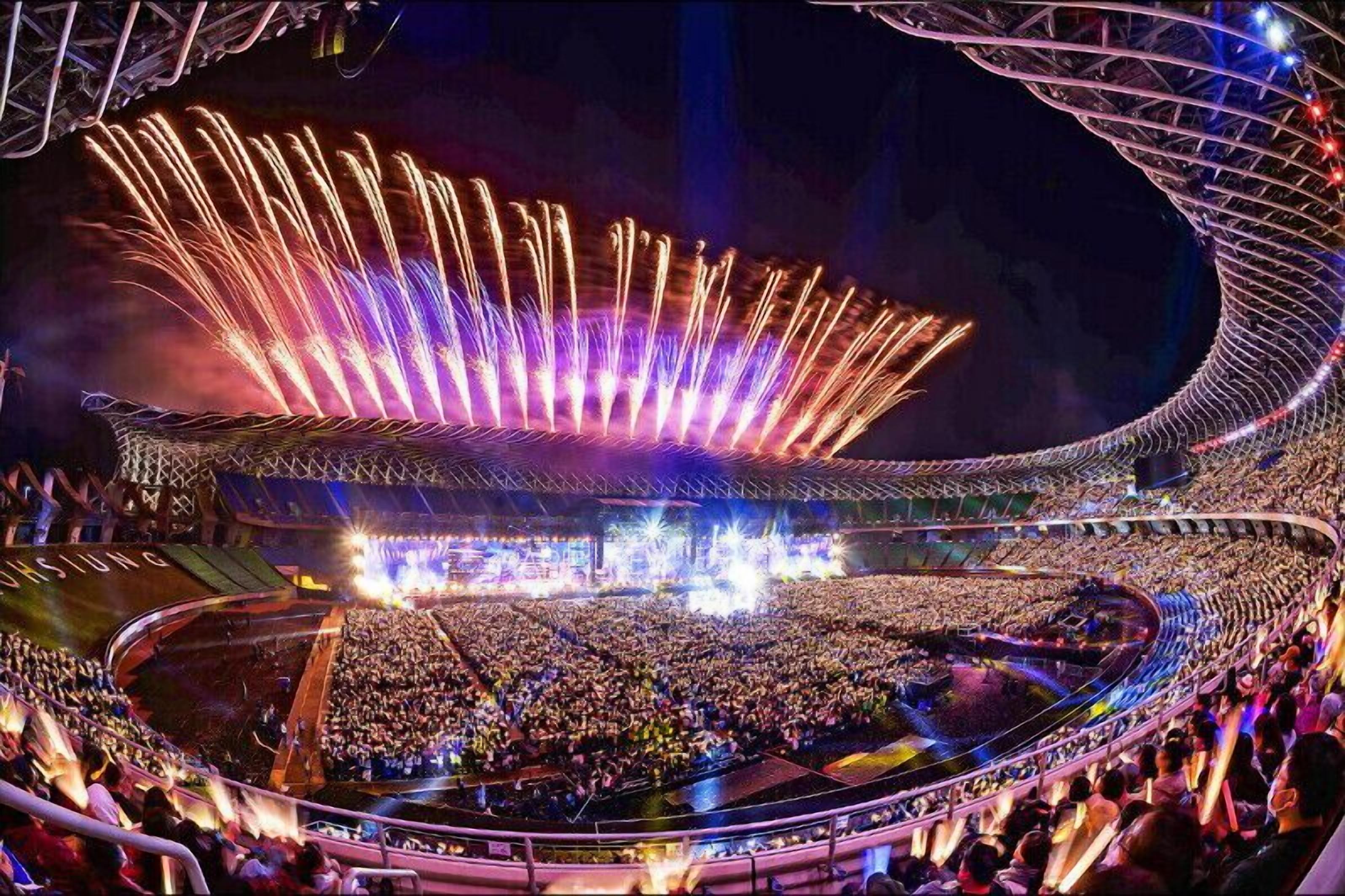 A large stadium with a curved roof structure and a crowd of people inside.