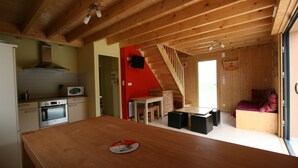 Une cuisine compacte dotée d’un plan de travail en bois, un coin repas avec une table et des chaises, et un escalier menant à une chambre à coucher avec un lit.