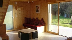 Un intérieur en bois comprenant un canapé, une table et une porte-fenêtre coulissante donnant sur un espace extérieur.