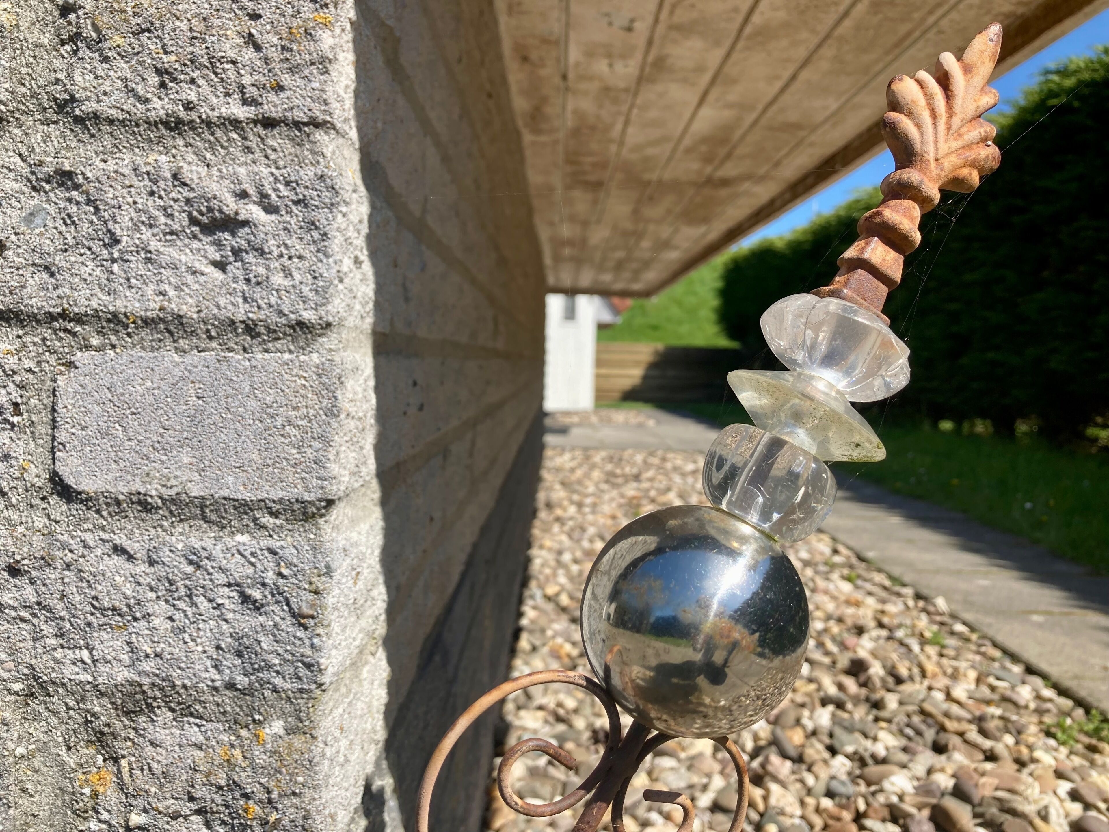 Een metalen sculptuur met een bladachtige bovenkant, een heldere bol en een reflecterende bol voor een stenen muur.