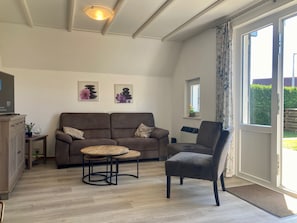 A living room with a sofa, armchair, round table, and a television on a cabinet. - Cozy Holiday home by the Dike in a Quiet Location at Lauwersmeer (Anjum)